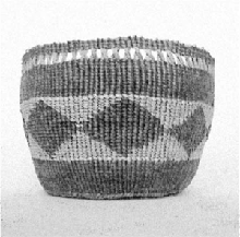 a black and white photograph of a basket with a diamond pattern woven by Sara Siestreem, with a plain background